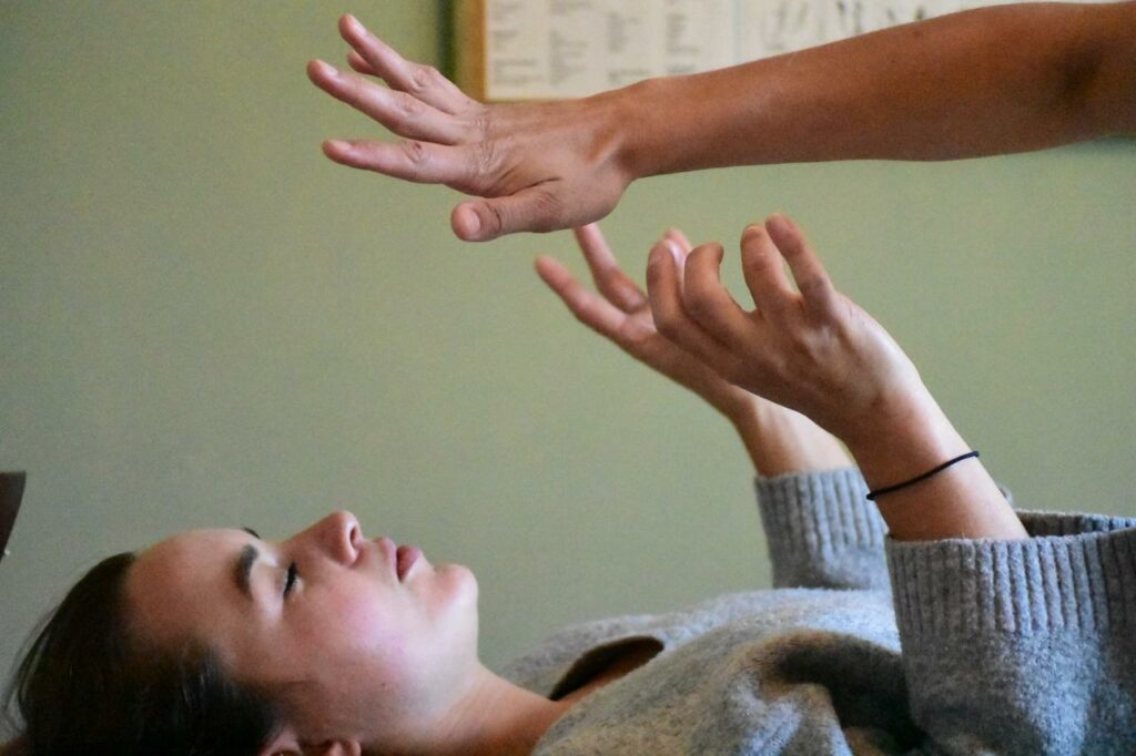 vue de la consultante allongée sur la table, les mains remontées au dessus du buste et vue seulement du bras de Camille qui surplombe le buste de la consultante