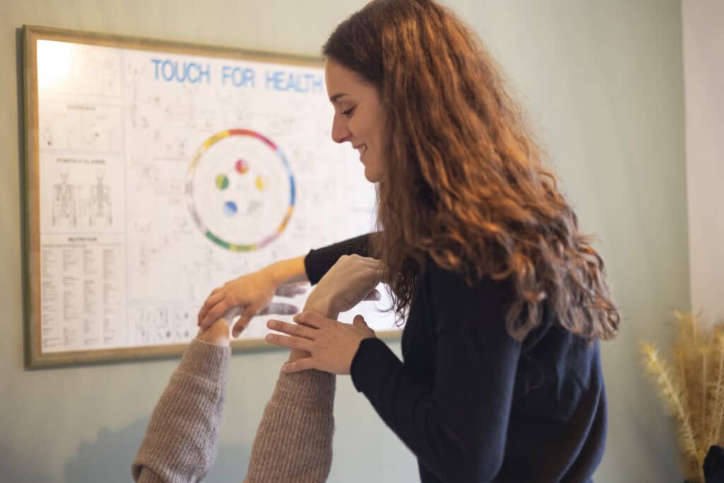 Camille qui travaille avec le sourire sur les poignets de son consultant dont on voit juste les bras levés