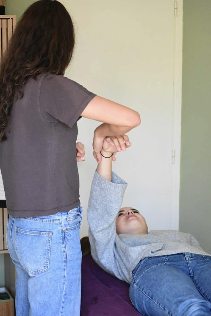 photo de Camille de dos entrain de pratiquer sur le poignet d'une consultante qui est allongée sur la table avec le bras en l'air
